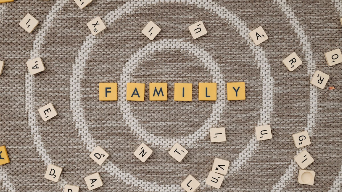 Scrabble tiles spelling 'family' on a textured brown surface, surrounded by scattered tiles.